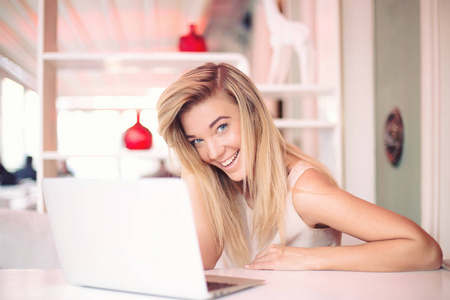 一个美丽快乐的年轻的微笑的女商人早上在一个舒适的咖啡馆工作的笔记本电脑