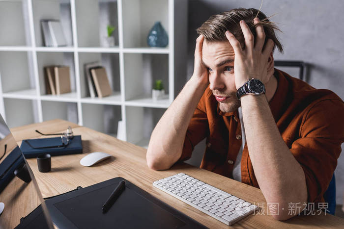 困惑的设计师坐在工作场所和手持头用手