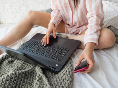 妇女在床上使用手提电话与计算机笔记本电脑