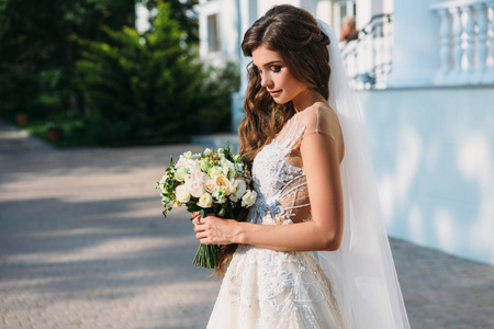 美丽的年轻新娘的肖像与可爱的打击白色婚纱礼服举行花束的花朵在她的手中。服装与家庭概念