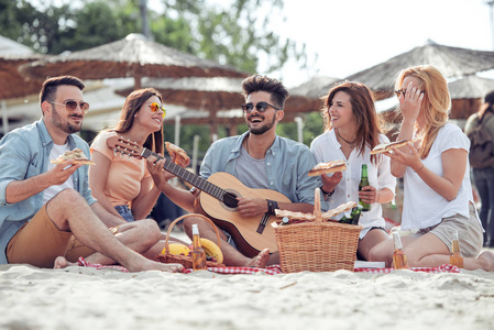一群朋友在海边玩得很开心, 吃比萨饼, 弹吉他, 享受
