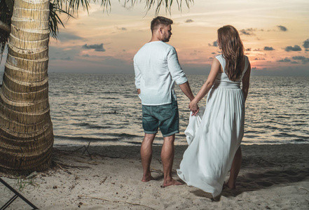 迷人的浪漫年轻夫妇在沙质热带海滩在美丽的日落