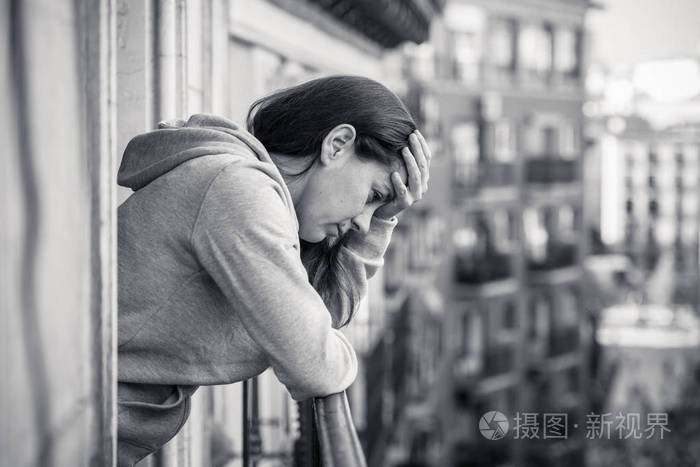 黑色和白色的悲伤不堪重负的妇女站在阳台上休息栏杆上的看法照片