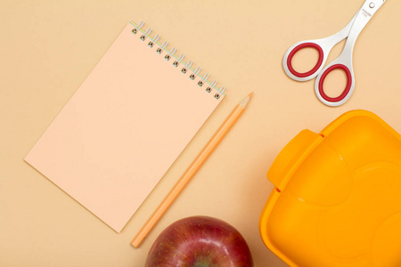 学校用品。笔记本, 彩色铅笔, 苹果, 剪刀和在米色背景的午餐盒。顶部视图。回到学校的概念。粉彩色