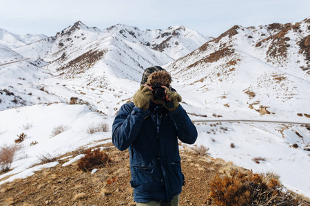 一个愉快的旅行者与照相机站立在被雪覆盖的山之中哈萨克斯坦