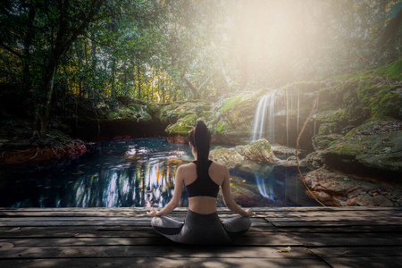 年轻女性在森林瀑布中做瑜伽冥想照片