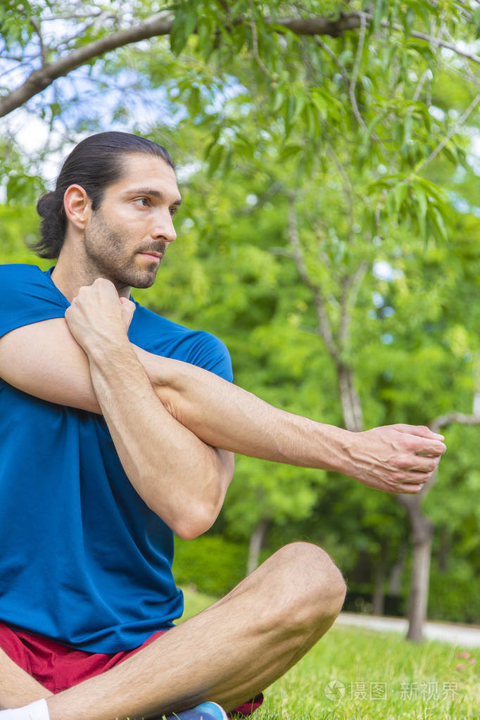 青年男子伸展双臂坐在草地上夏季公园