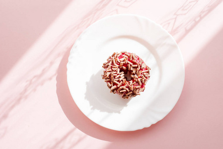 甜甜圈覆盖红釉, 并洒在粉红色背景下的白色板上的磨碎巧克力与表面图案的阴影