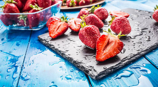 新鲜成熟的草莓用清水冲洗在蓝桌上