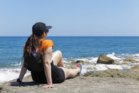 一个女人的前景, 对太阳的帽子, 休息在海滩上的岩石寻找大海