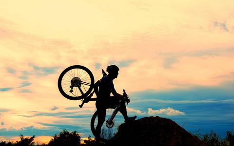 骑单车骑自行车的人在山顶上的草地上日落时的剪影迎接胜利的挑战
