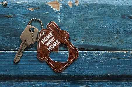 房子钥匙在房子形状的钥匙链上休息在木背景, 概念为不动产