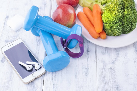 运动器材, 蓝色哑铃和水果, 蔬菜和电话。音乐用的健身手镯和耳机。书写文字或广告的自由空间