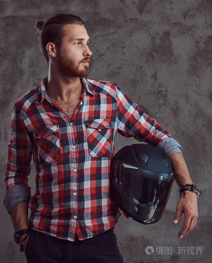 一个年轻英俊的红发摩托车穿着法兰绒衬衫持有摩托车头盔在灰色背景