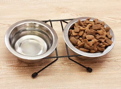 狗干的食物和水中金属碗木制背景上