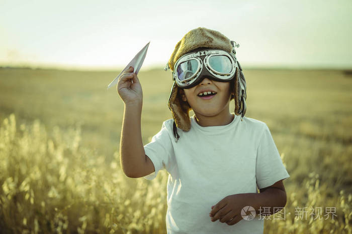 快乐的男孩在日落时扮演飞行员, 他戴着飞机的飞行员眼镜和一些纸板像翅膀