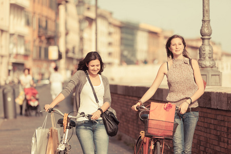 行走在城市与自行车和袋中的两个漂亮女人