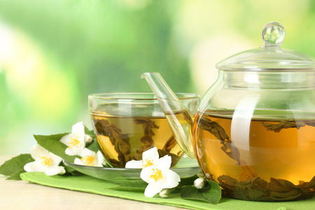 绿茶与茉莉花在杯子和绿色背景上的木桌上的茶壶照片