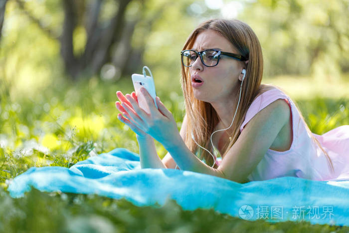 女孩放下或放松在绿色草听音乐与智能手机在夏天或春天