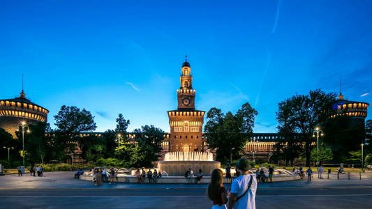 主入口的广场城堡和塔卡斯特罗斯福尔扎照亮天到夜间过渡时差, 米兰, 意大利。喷泉和人走动