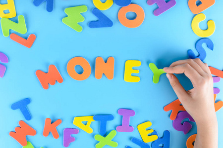 美丽的不寻常的背景。这个女孩用五颜六色的字母把钱用词放了出来。