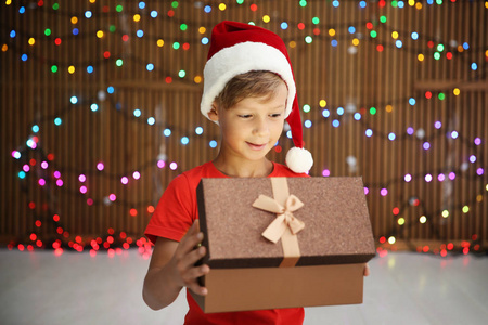 可爱的小孩子在圣诞老人的帽子打开圣诞礼物盒在模糊的灯光背景
