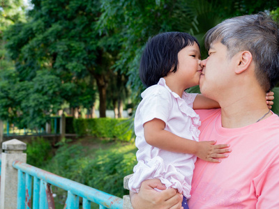 女儿在父亲的怀抱中, 用爱亲吻对方。亚洲家庭与爱情概念