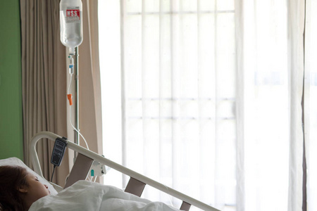 妇女病人躺在医院床上用手接受盐水液滴注治疗液体置换治疗的窗口和阳光。医疗保健理念