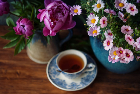 美丽的花朵在花瓶和杯茶在木桌。选择性聚焦