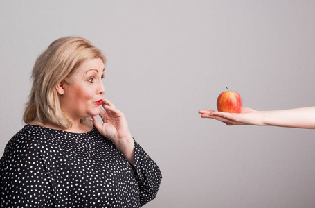 女性手给一个苹果在工作室的一个有吸引力的超重妇女