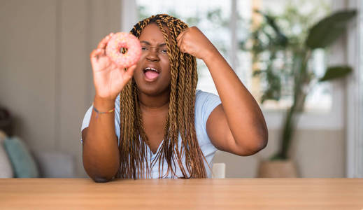 非洲裔美国妇女吃甜甜圈懊恼和沮丧的呼喊与愤怒, 疯狂和叫喊与举手, 愤怒的概念