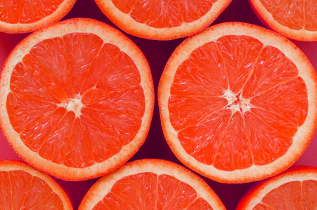 在明亮的背景粉红色的一些柚子切片的顶部视图。饱和柑橘纹理图像