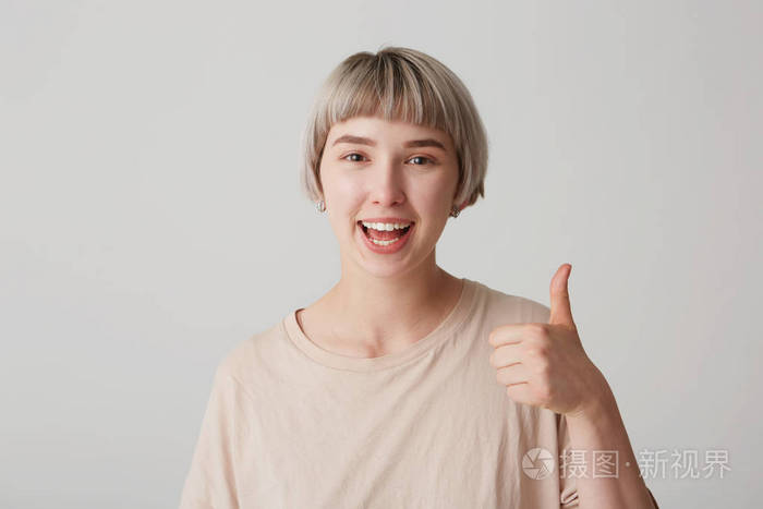 室内拍摄的微笑年轻女孩保持大拇指, 显示她的同意或协议, 隔离在白色