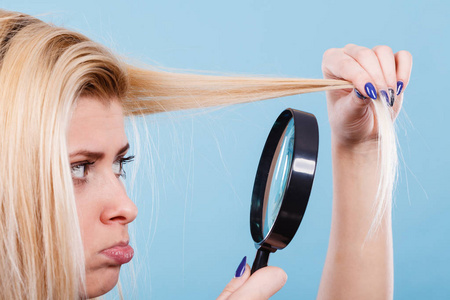护发和发型设计，漂白概念的不良影响。金发女人看着头发受损 分裂结束通过放大镜
