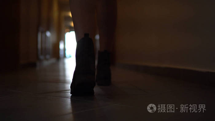 跟随无法辨认的妇女在黑暗的走廊的人行道上走在靴子的脚步