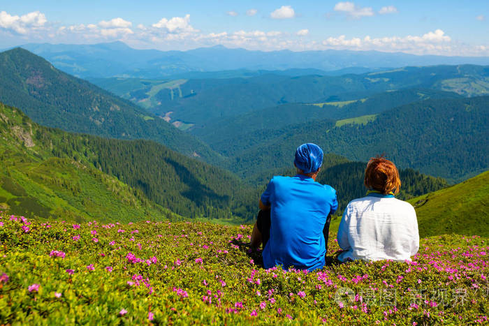 幸福的情侣是放松和享受生活在绿色的山坡上盛开的粉红色杜鹃在伟大的