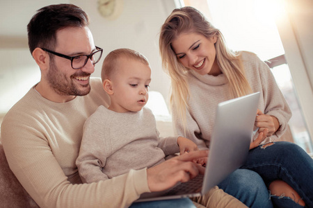 微笑的父母和他们的小儿子在家里使用笔记本电脑