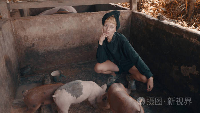 美丽的时尚女孩喂养小猪和摆在小脏猪农场.时尚时髦女性肖像