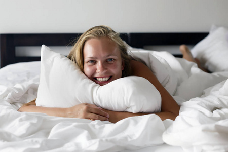 年轻美丽快乐的女人躺在床上, 一个白色的 knicker 醒来后, 对观众微笑