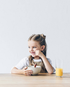 快乐的小女孩与碗早餐和橙汁隔绝白色