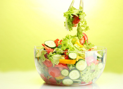 新鲜蔬菜沙拉中透明碗用勺子和叉子上绿色背景
