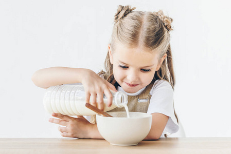 快乐的小女生把牛奶倒入谷物早餐隔离白色