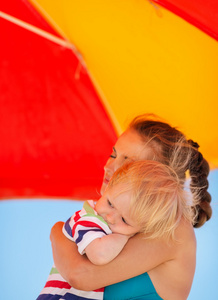 妈妈抱抱宝宝在伞下的海滩上