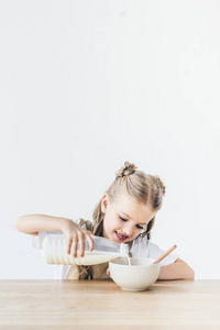 微笑的小女生把牛奶倒入谷物早餐隔离白色