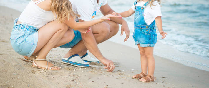 关闭幸福的家庭三美丽的妻子, 父亲和女儿在海滩上漫步在日落的乐趣。家庭旅游理念