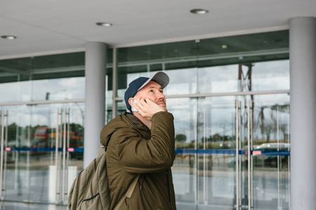 一个年轻的男性游客在机场或附近的购物中心或车站打电话给出租车或交谈的手机或与朋友交流使用手机