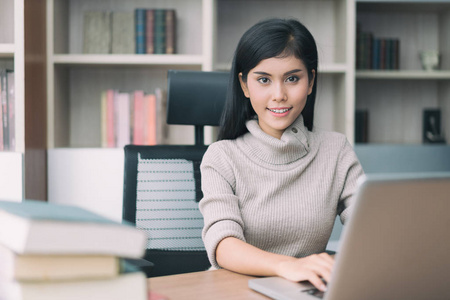 亚洲年轻聪明的女人与休闲做她的笔记本电脑的业务工作和坐在椅子上在经理室经理