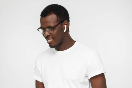 特写图片的英俊的非洲男子站在灰色背景下, 看着通过眼镜有时髦的耳机没有线的享受音乐和思考他的一些想法