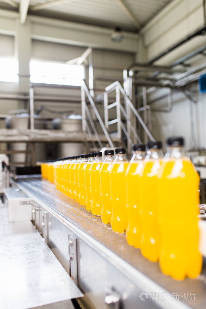工业工厂在室内和机械机器人工厂流水线生产和装瓶的苏打水和橙果汁瓶