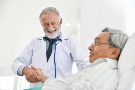 幸福的人。高级男医生正在医院的医疗室与亚洲男性病人交谈和握手。微笑